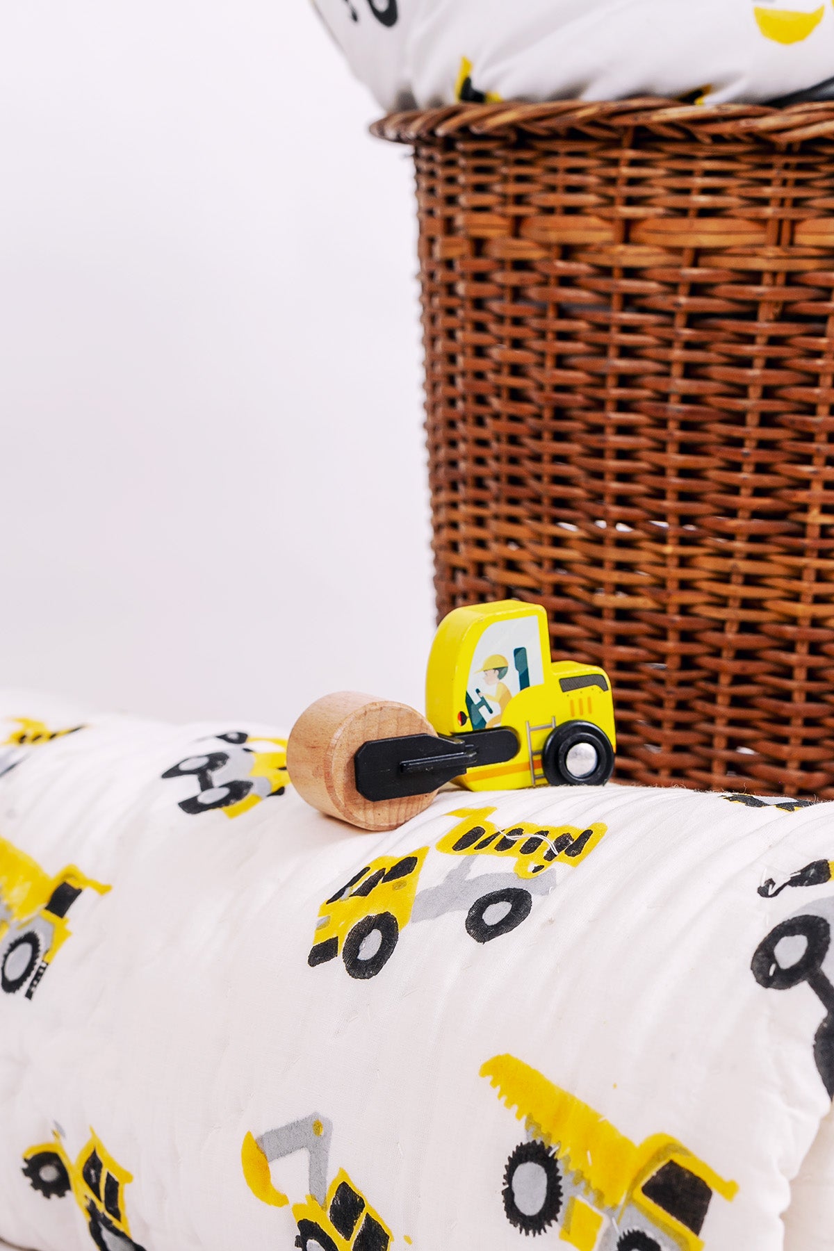 Close-up of hand block printed yellow construction trucks on cotton mulmul baby quilt with wooden toy road roller