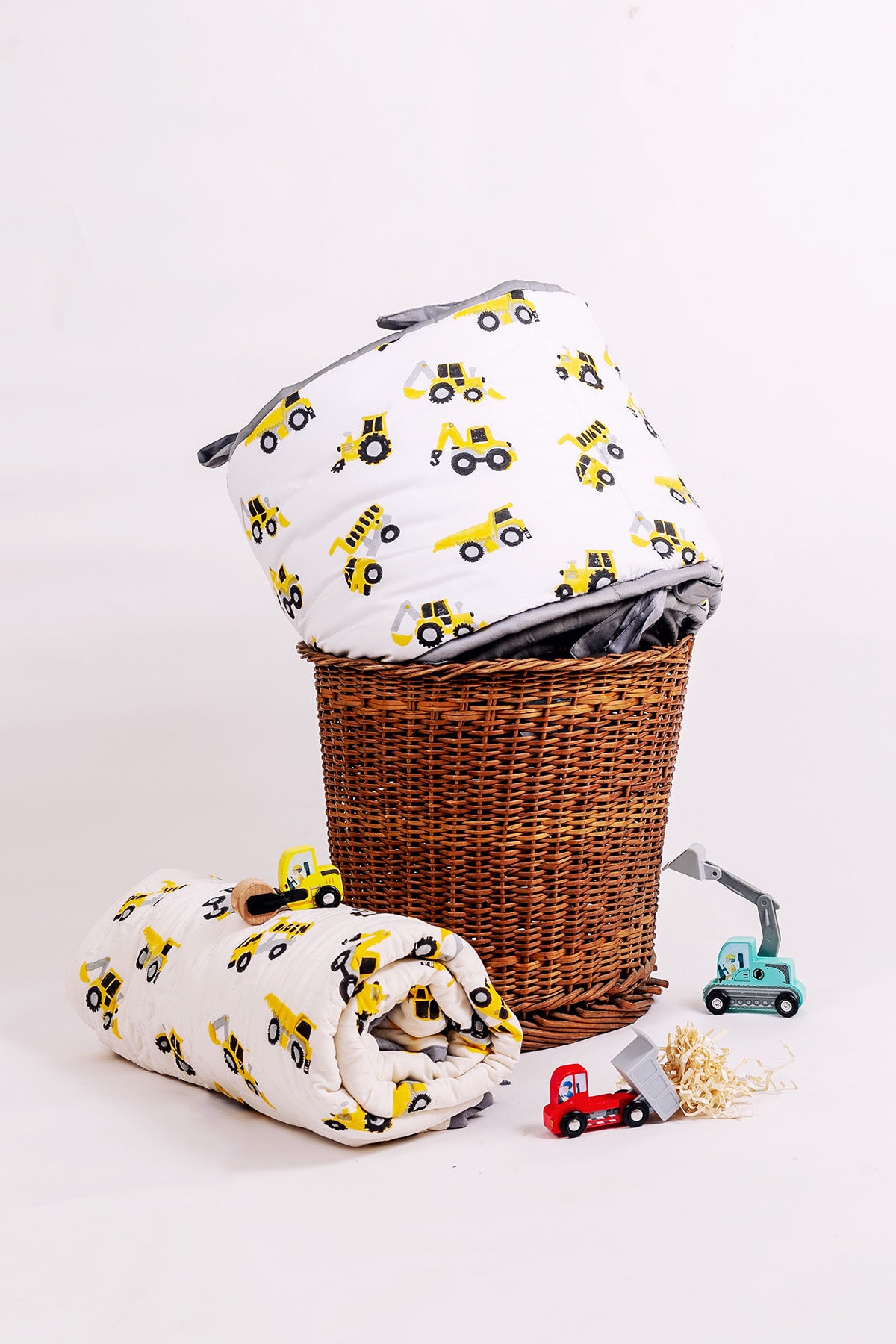Construction truck print cot bumper on a wicker basket with matching rolled baby quilt and toy trucks