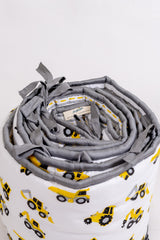 Top view of rolled construction truck crib bumper showing grey fabric ties, striped reverse and Bumblebee label